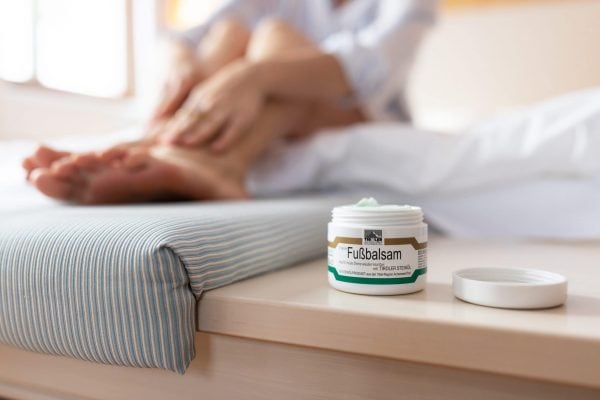 Fußbalsam auf Tisch mit entspannenden Füßen