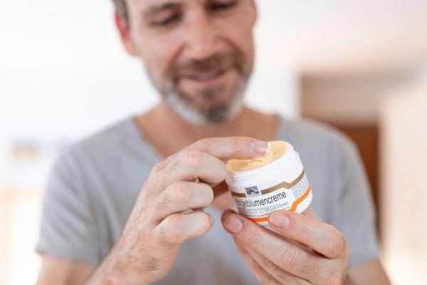 Mann verwendet Hautpflegecreme aus einem Behälter.